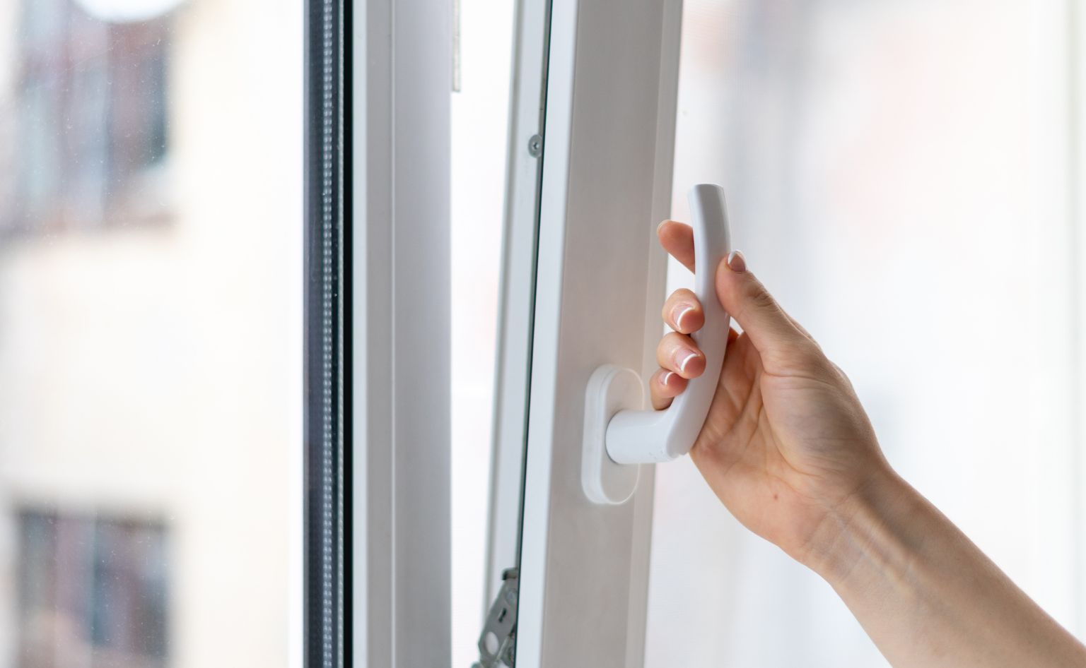 Hand opent wit raam in zonnige kamer.